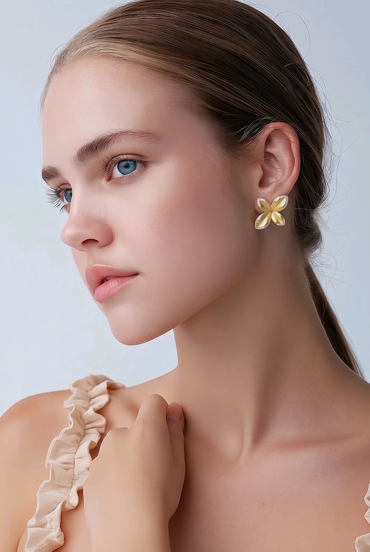 Aros Ámbar Joyas en forma de flor de cuatro pétalos con baño de oro 18k y textura granulada puestos en una modelo.